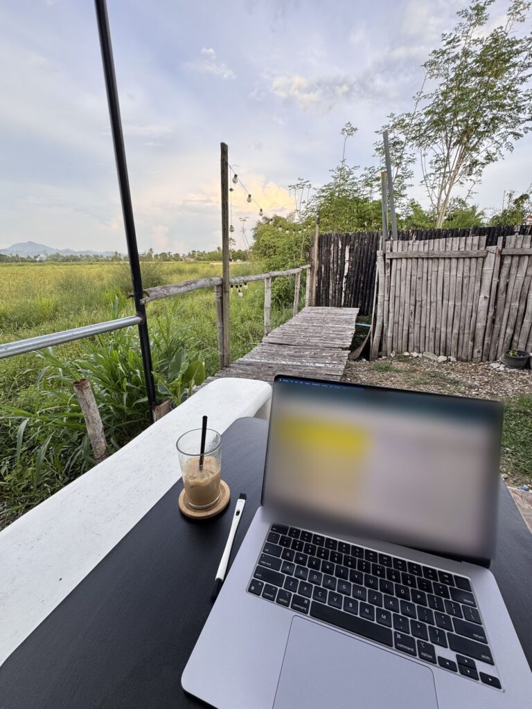 Laptop and iced coffee on an outdoor work table at Arbs Co&Co, overlooking the rice fields